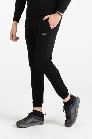 Full-body view of a man wearing a black Versace 19.69 tracksuit set with silver 19V69 linear branding on the joggers.